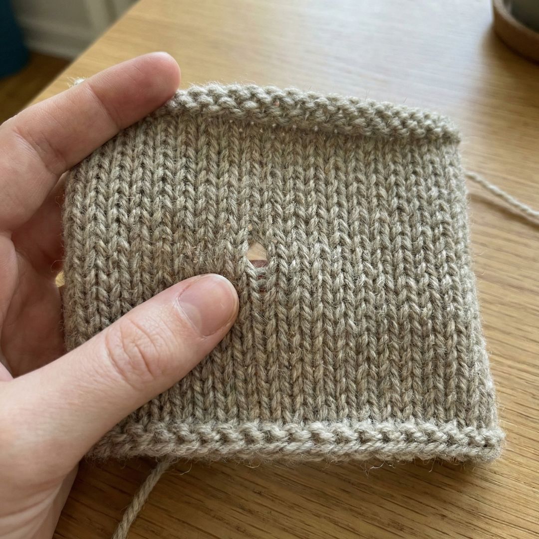 Close-up of an accidental yarn-over hole in a knitted project, illustrating how to scan for errors.